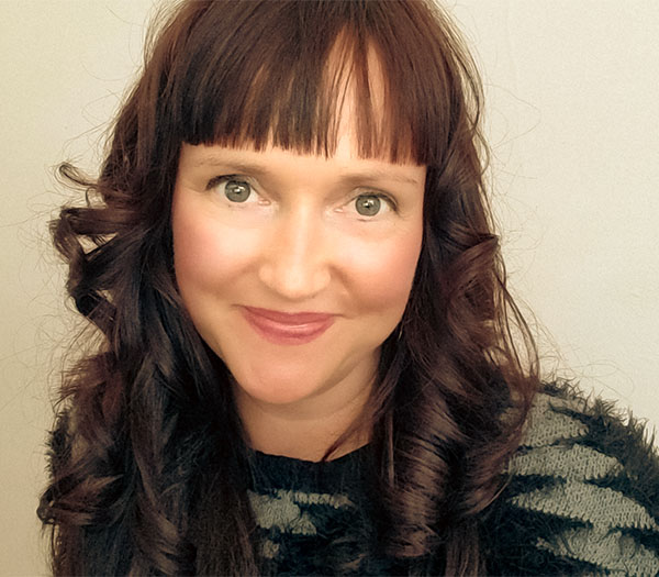 Photograph of woman with long brown hair and patterned sweater (Pamela French) smiling directly into the camera.